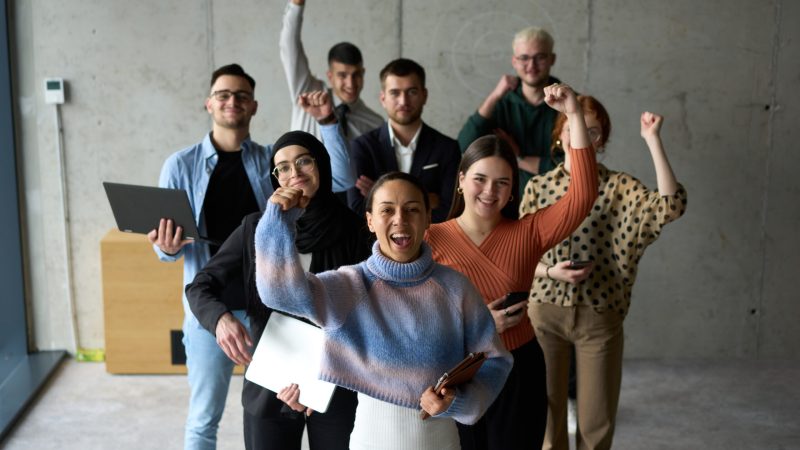 A diverse team of business professionals ecstatically celebrating their success in a modern office, expressing triumph and unity after achieving their goals