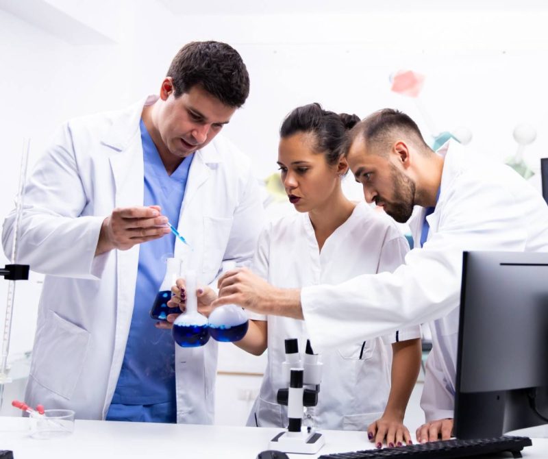 team-scientist-white-coat-working-together-with-smoking-blue-liquid-modern-research-lab