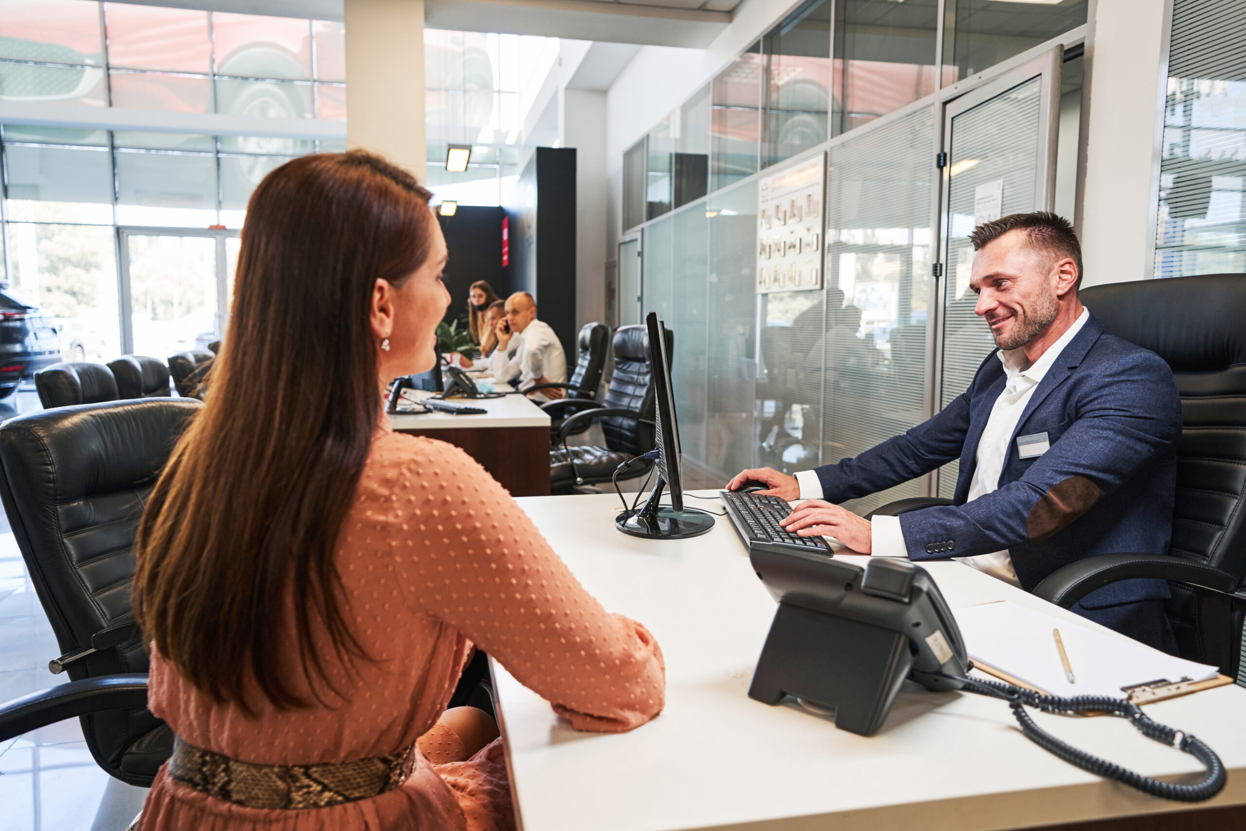 Woman sitting at the table in front of a cheerful man in a car showroom and talking to him